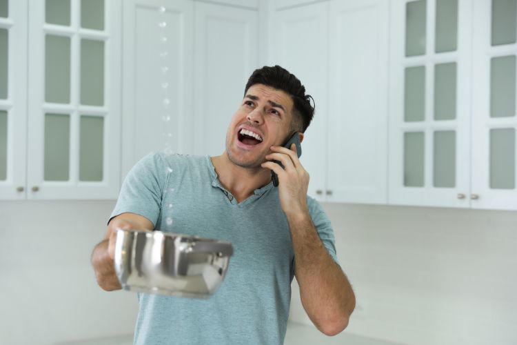 Anxious man collecting water from leaking roof while on a call